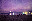 A nighttime beach scene under a vibrant purple sky. Silhouettes of people on the beach contrast with the lights reflecting on the water. blurred out low res